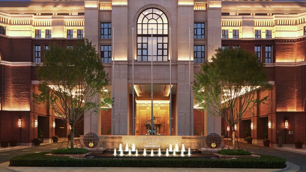 Un hotel con una entrada arqueada destacada, una fachada bien iluminada y una fuente al frente.