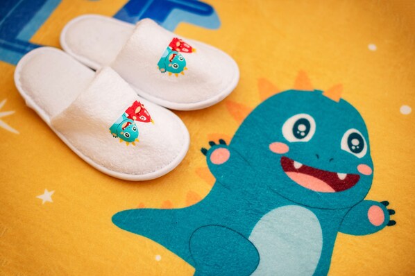 Un par de pantuflas blancas con personajes de dibujos animados y un dinosaurio de peluche sobre una superficie colorida.