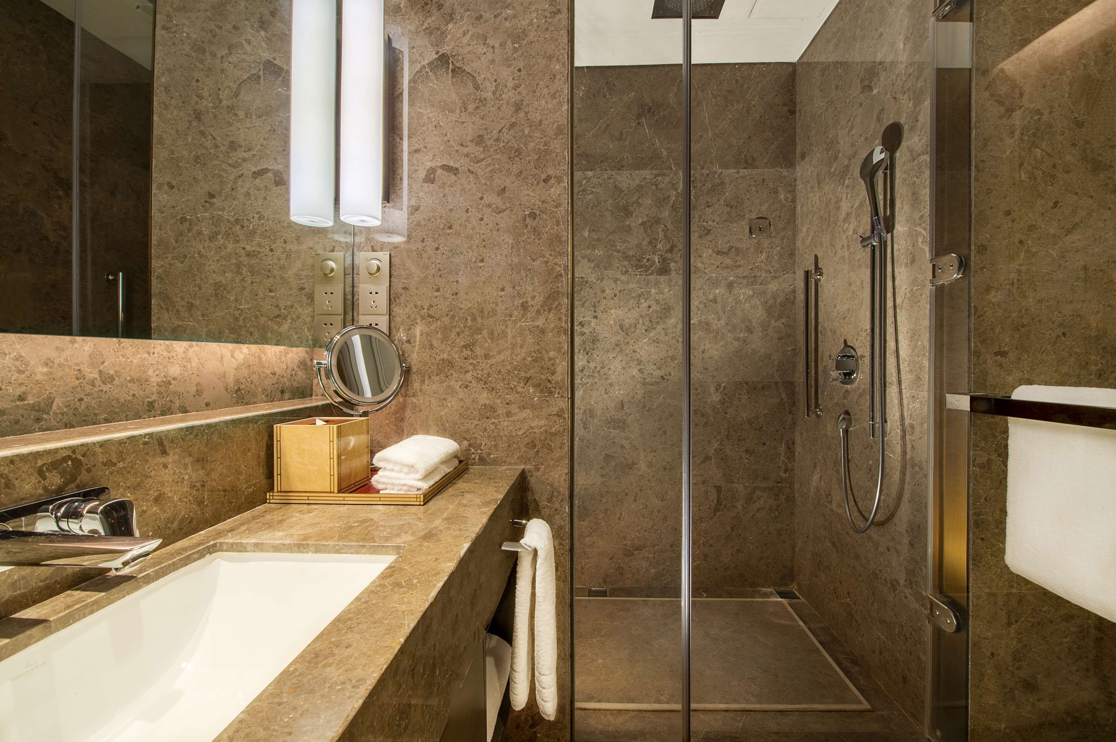 Un baño moderno con ducha de vidrio, un espejo grande y encimera de mármol.