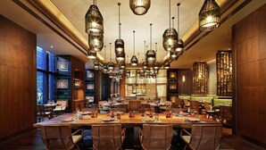 Un comedor amplio con una larga mesa de madera dispuesta para varios comensales, rodeado de sillas de mimbre.
