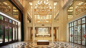 Un lobby espacioso con una gran araña, una zona de estar central y amplios ventanales con paneles de vidrio decorativos.