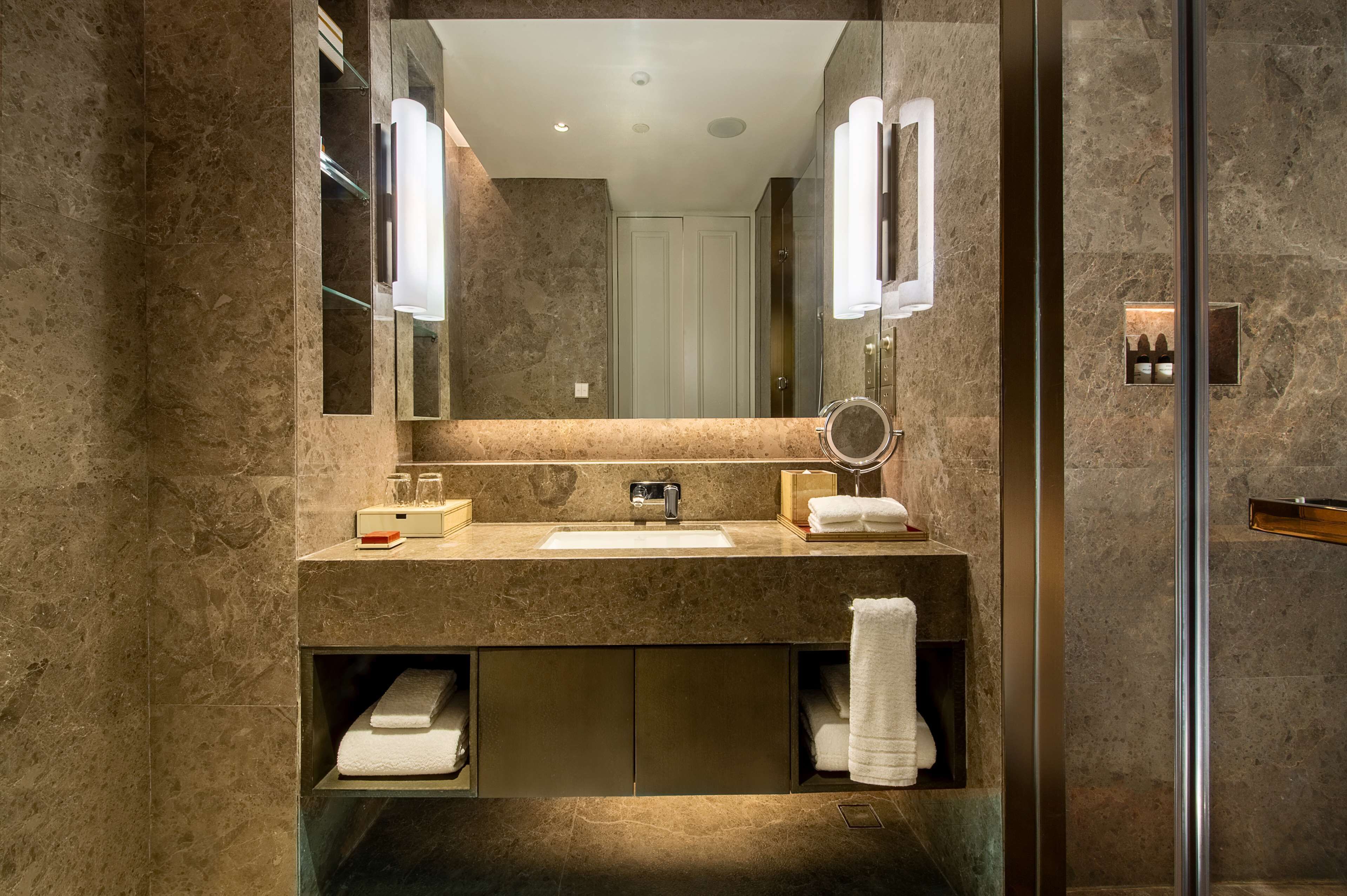 Un baño moderno con encimera de mármol, lavamanos, espejo y estantes empotrados para toallas.