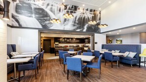 Un restaurante con un mural de cascada, asientos azules y una zona de cocina al fondo.