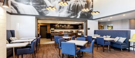 Un restaurant décoré d’une fresque représentant une cascade, avec des sièges bleus et une cuisine visible au fond de la salle.