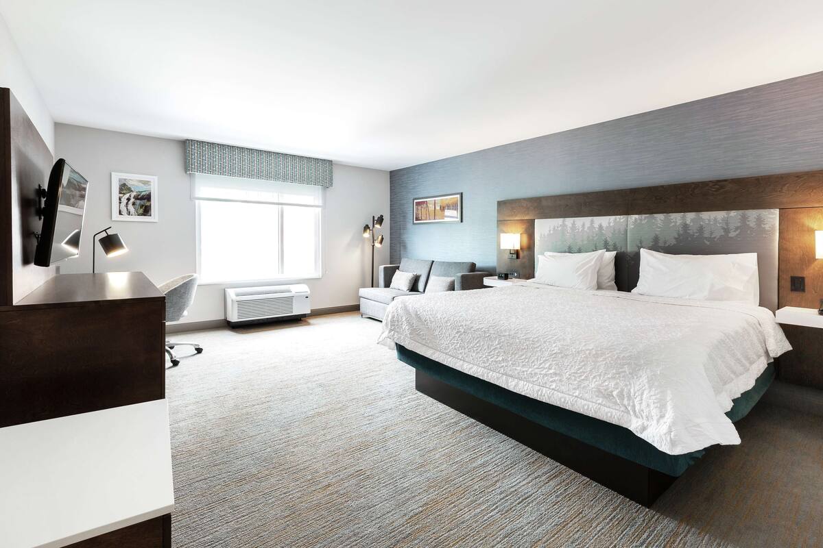 A modern hotel room with a large bed, a desk, and a flat-screen TV.