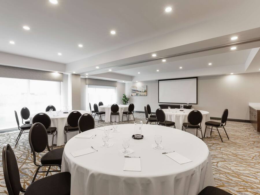 Une salle de conférence équipée de tables rondes, de chaises et d’un écran de projection.