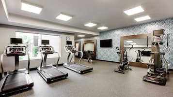 Un gimnasio con cintas de correr, bicicletas estáticas y una máquina de remo.
