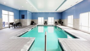 Una piscina interior con agua azul cristalina, rodeada de paredes con azulejos e iluminación empotrada en el techo.
