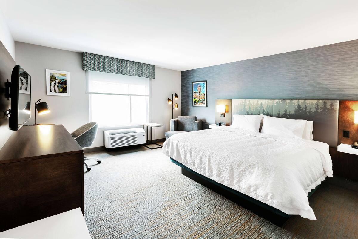A modern hotel room with a large bed, a desk, a chair, and a flat-screen TV.