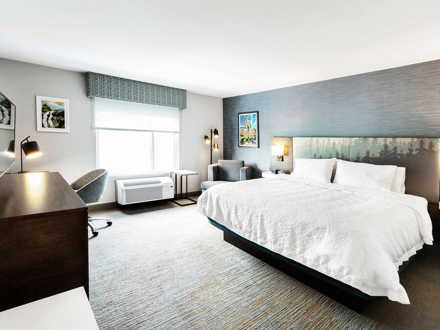 Una habitación de hotel moderna con una cama grande, un escritorio, una silla y un televisor de pantalla plana.