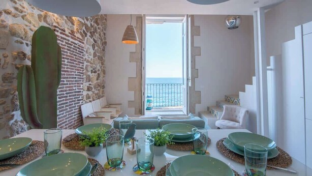 A dining area with a table set for four, a stone wall, and a balcony with a view. - Lio loft, romantic and stunning sea view apt (Syracuse)