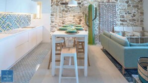 A modern kitchen with a stone wall, a dining table set for four, and a light blue sofa in the living area. - Lio loft, romantic and stunning sea view apt (Syracuse)