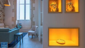 A modern living room with a sofa, armchair, and a small table. There are framed artworks on the wall and a decorative plate in a display case. - Lio loft, romantic and stunning sea view apt (Syracuse)