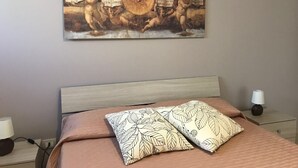 A bedroom with a bed, pillows, a nightstand, a lamp, and a wall-mounted painting. - villa in San Leone with swimming pool (san leone agrigento)