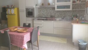 A compact kitchen with white cabinets, a yellow refrigerator, a dining table with a red and white tablecloth, and a trash bin. - villa in San Leone with swimming pool (san leone agrigento)