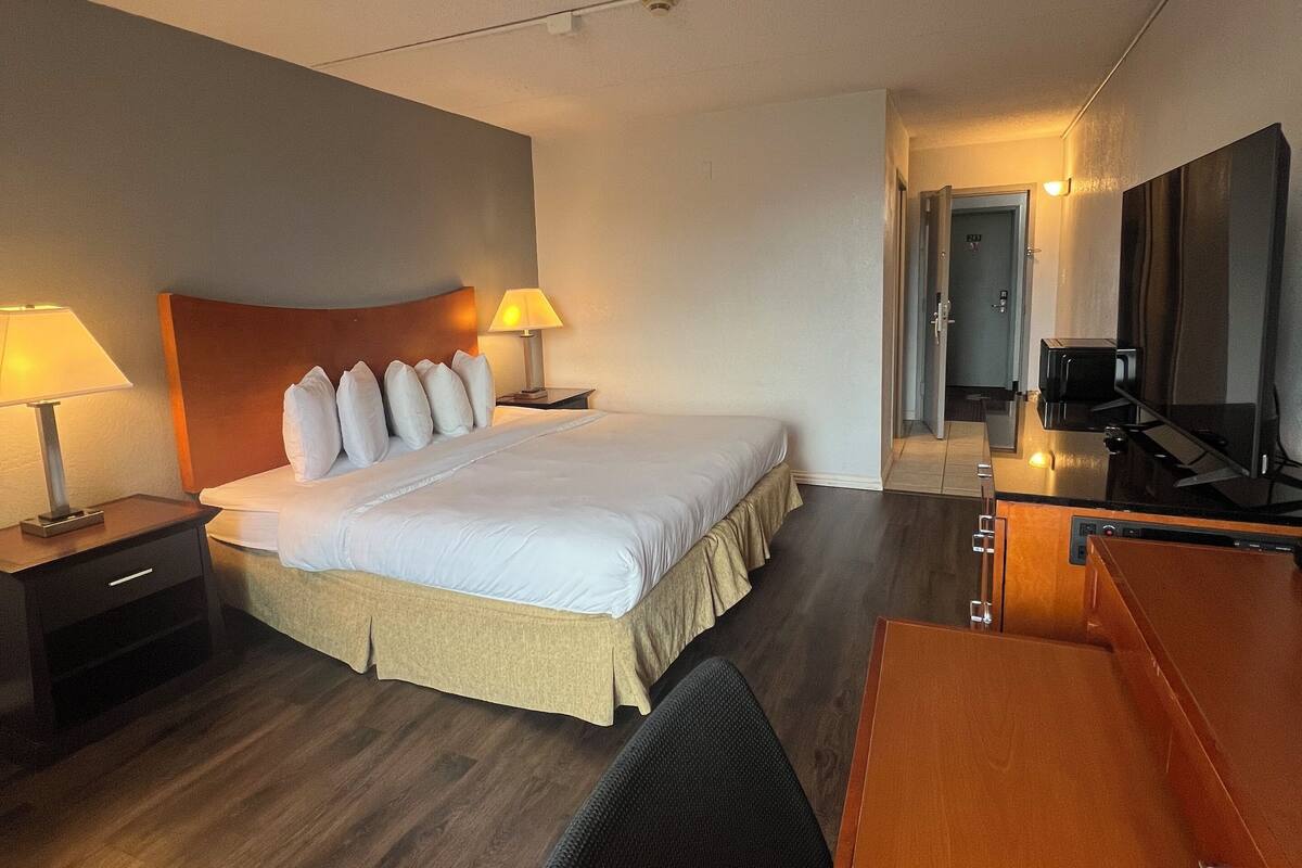 A hotel room with a bed, bedside lamps, a desk, a chair, and a television.