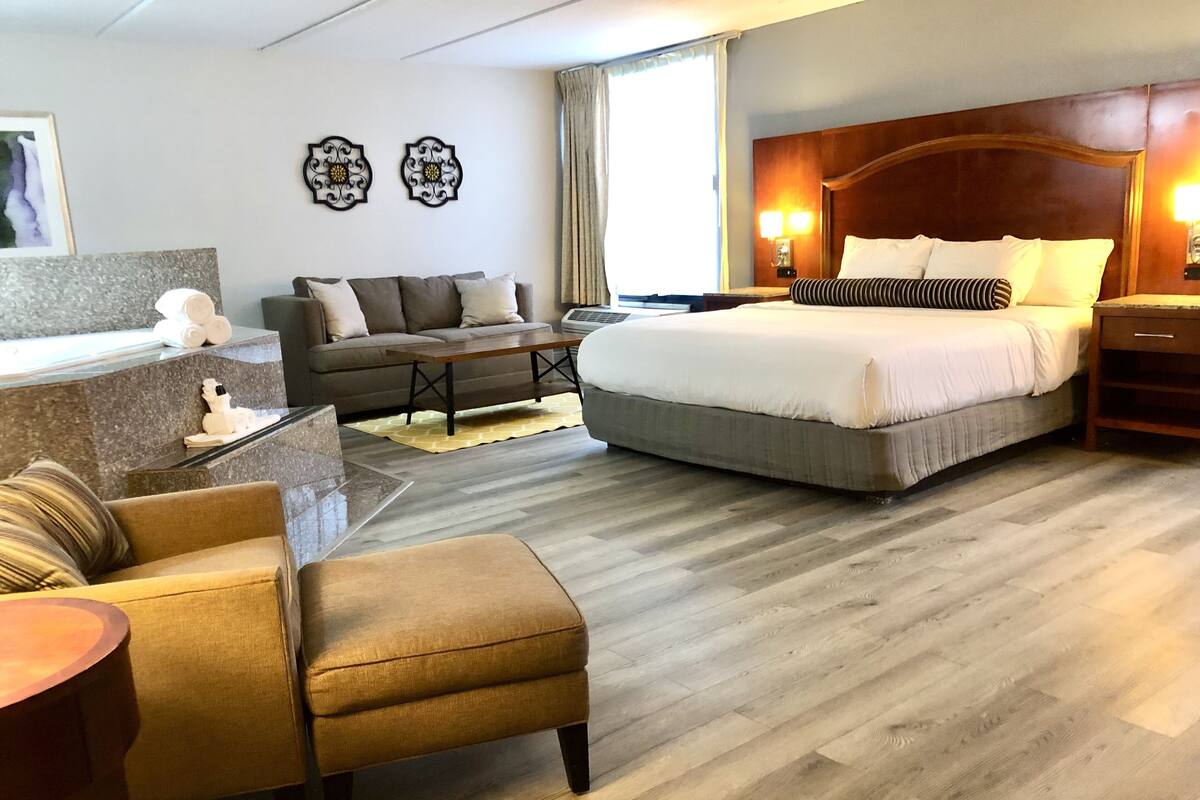 A hotel room with a bed, a sofa, a small table, a desk, and a chair.