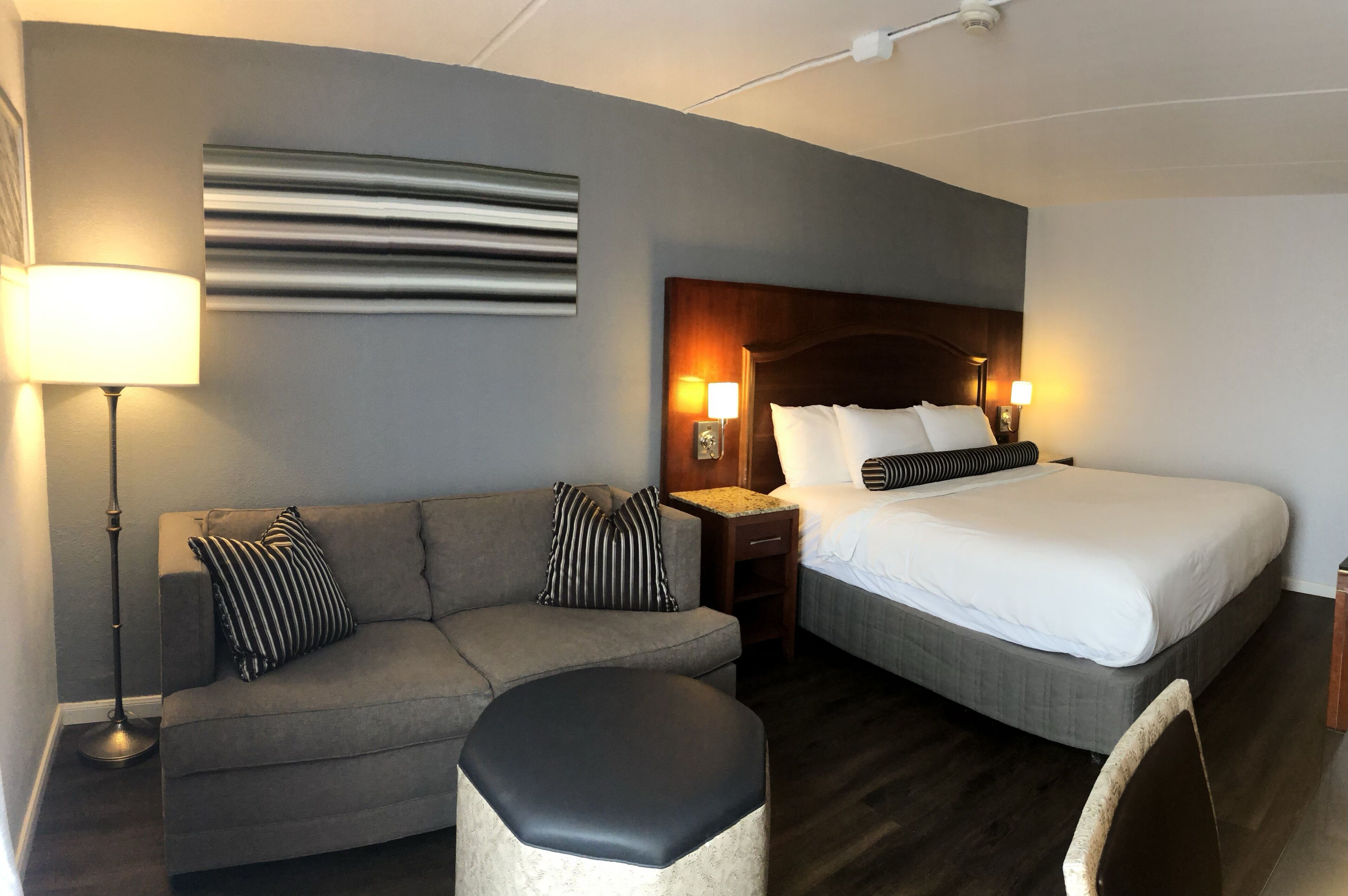 A hotel room with a bed, a sofa, a nightstand, and a lamp.