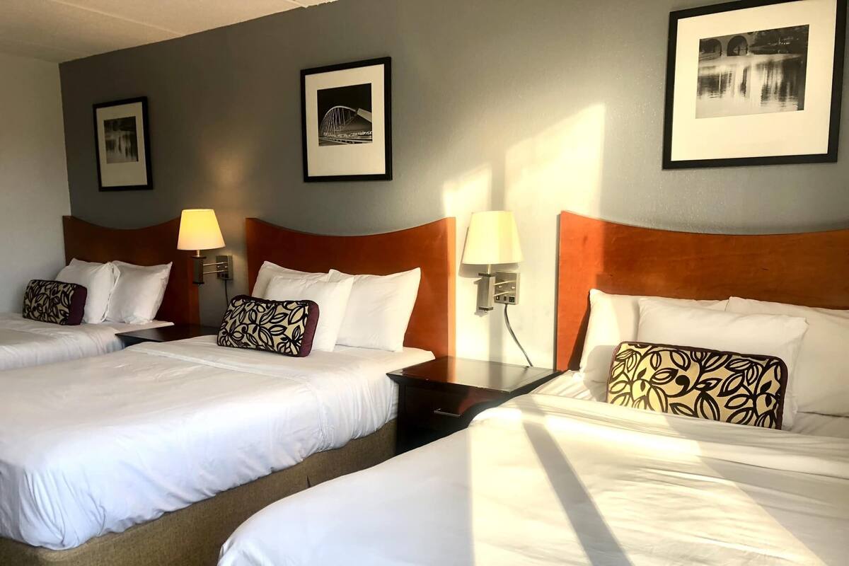 A hotel room with two beds, each with white linens and patterned pillows, a wooden headboard, and framed pictures on the walls.