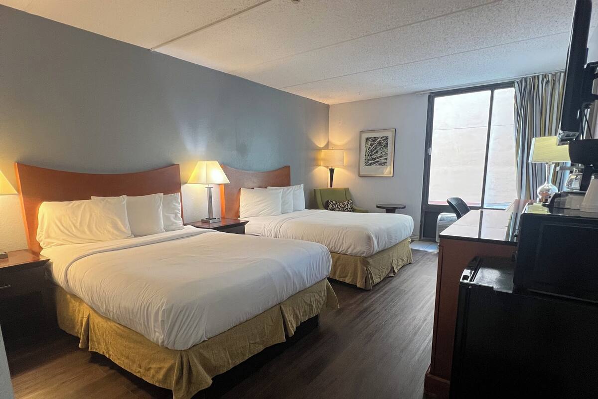 A hotel room with two beds, a desk, a chair, a TV, and a window.
