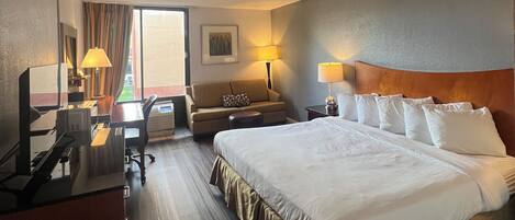 Habitación de hotel con una cama grande, un escritorio con computadora, un sofá y una ventana con cortinas.