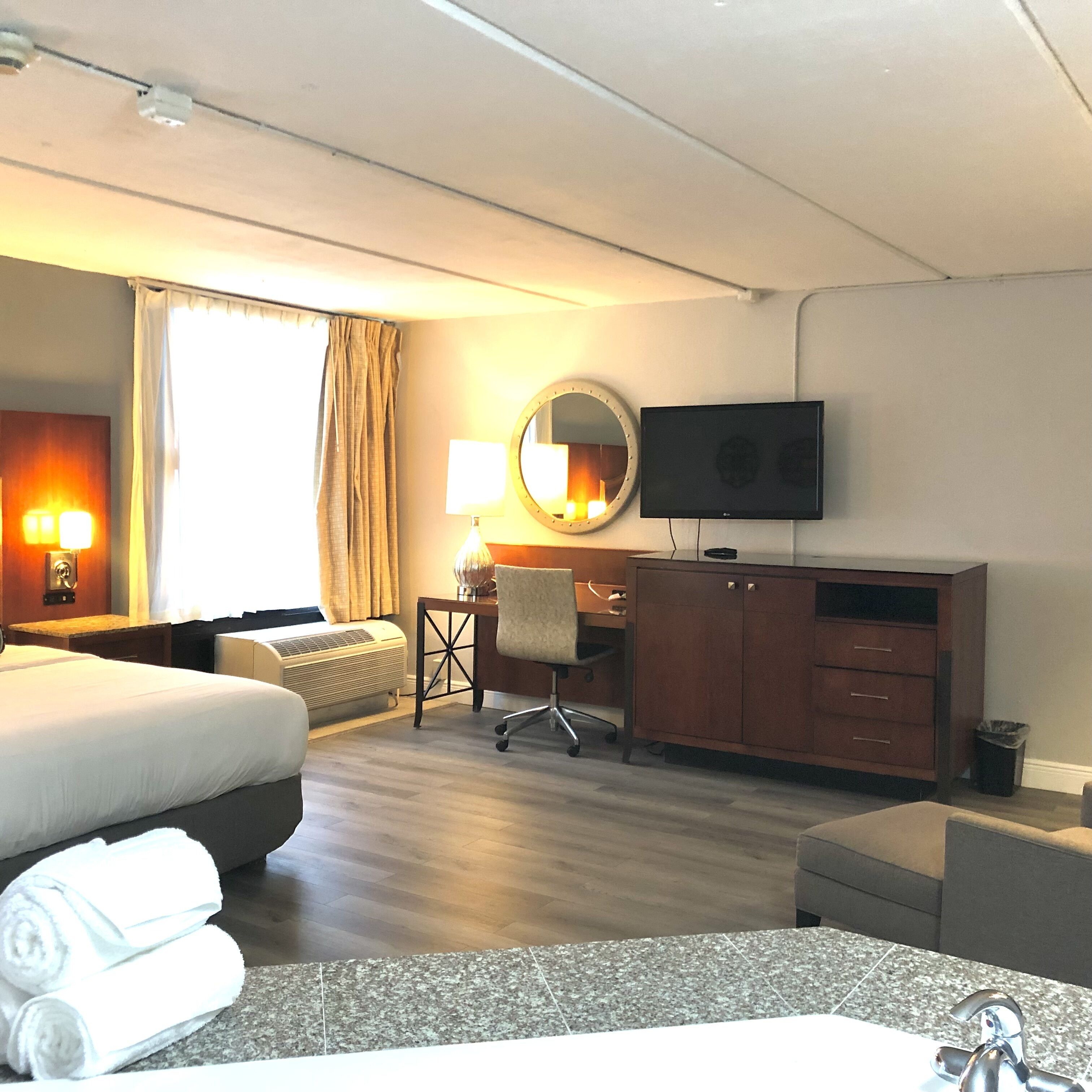 Une chambre d’hôtel équipée d’un lit, d’un bureau, d’une chaise, d’une télévision et d’une salle de bain avec un lavabo et un miroir.