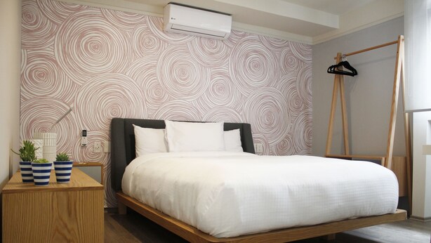 Een slaapkamer met een bed, een houten nachtkastje, een wandairconditioner en een houten kledingrek.