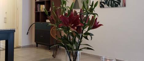 Una sala de estar moderna con una mesa de centro de vidrio, un florero con flores rojas, una vela encendida y arte abstracto en la pared.