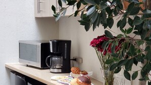 Een kitchenette met een magnetron, koffiezetapparaat en een klein zithoekje met stoelen.