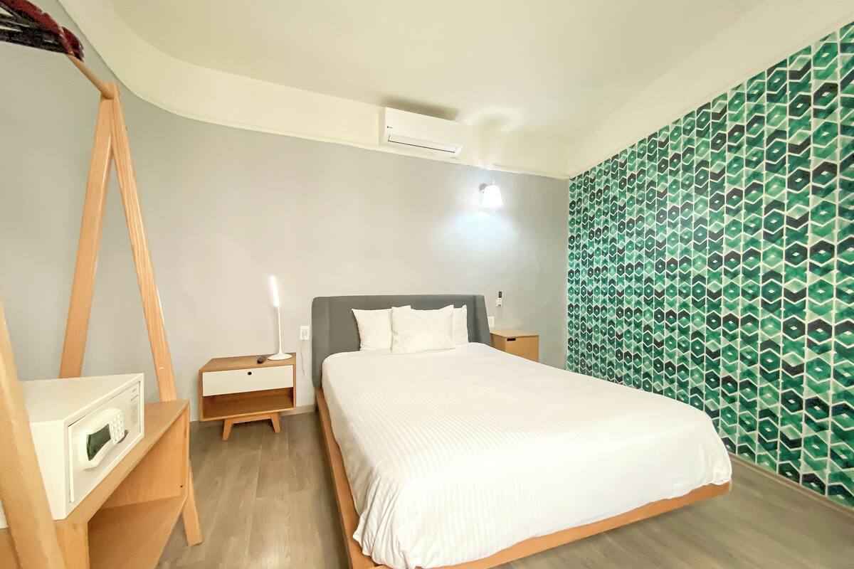 Een slaapkamer met een bed, een nachtkastje, een lamp, een wandairconditioner en een behangen muur.