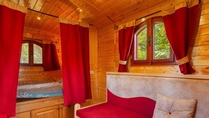Une pièce de cabane en bois comprenant un lit, une fenêtre avec des rideaux et un canapé avec un coussin.