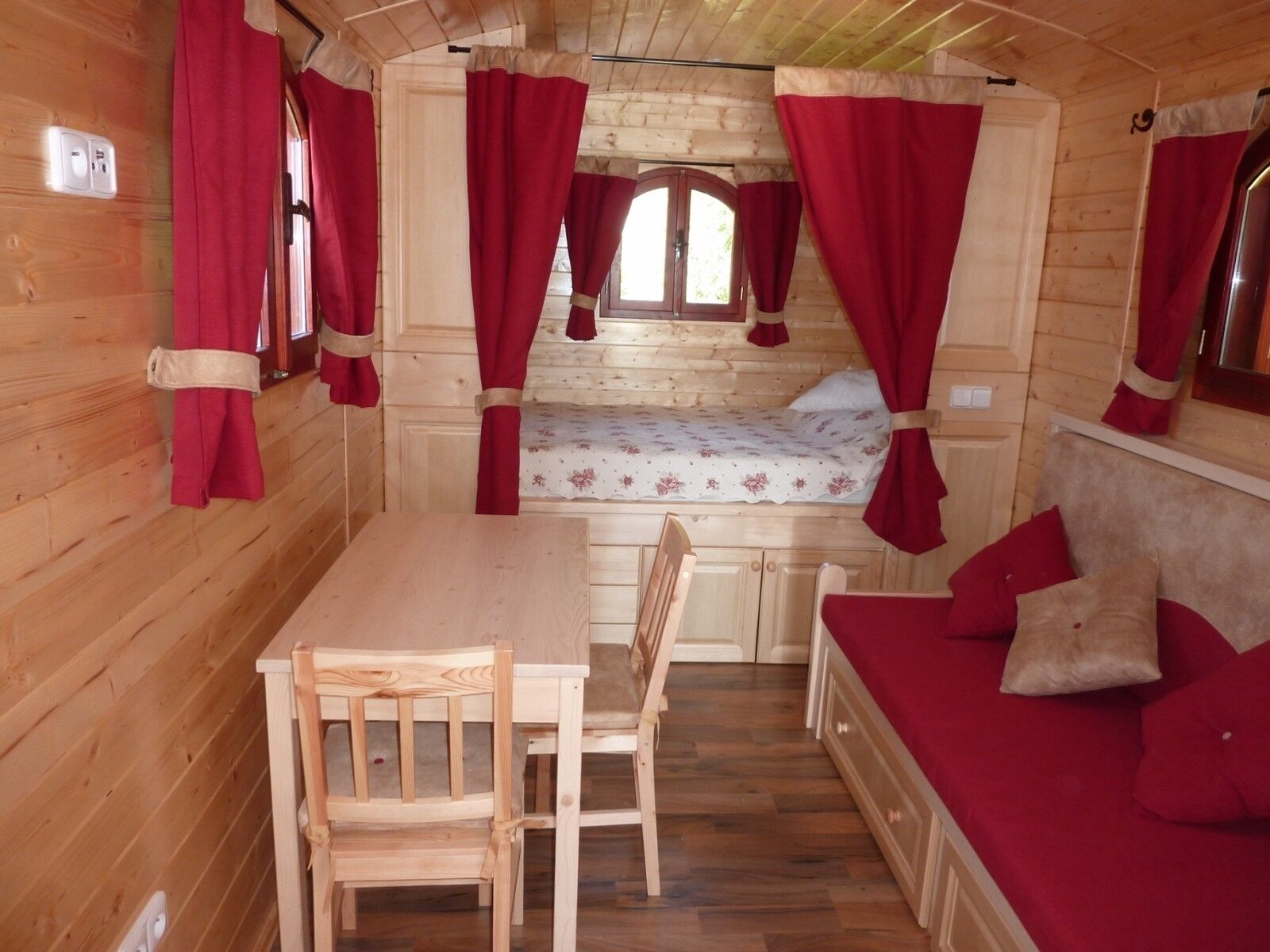A wooden cabin interior with a bed, a table, and chairs.