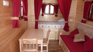 A wooden cabin interior with a bed, a table, and chairs.