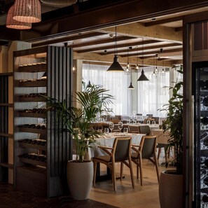 A dining area with wooden tables and chairs, potted plants, and pendant lighting. - Marea Valamar Collection Suites (Porec)