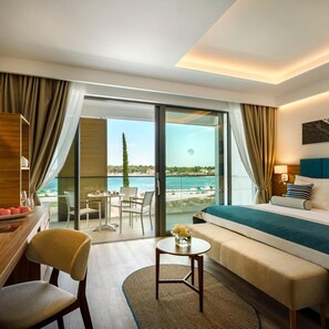 A hotel room with a bed, a desk, a chair, a small table, and a view of the sea. - Marea Valamar Collection Suites (Porec)