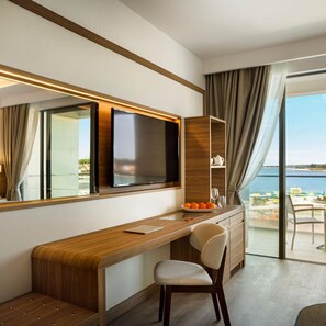 A modern hotel room with a wooden desk, a television, and a view of the sea. - Marea Valamar Collection Suites (Porec)