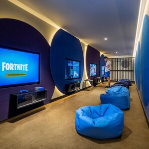 A gaming lounge with multiple screens displaying video games, bean bags for seating, and a person using a tablet. - Marea Valamar Collection Suites (Porec)
