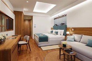 A modern hotel room with a bed, a desk, a chair, a sofa, and a small table.