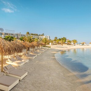 A beach resort with sun loungers and thatched umbrellas, a clear sky, and a hotel building in the background. - Marea Valamar Collection Suites (Porec)