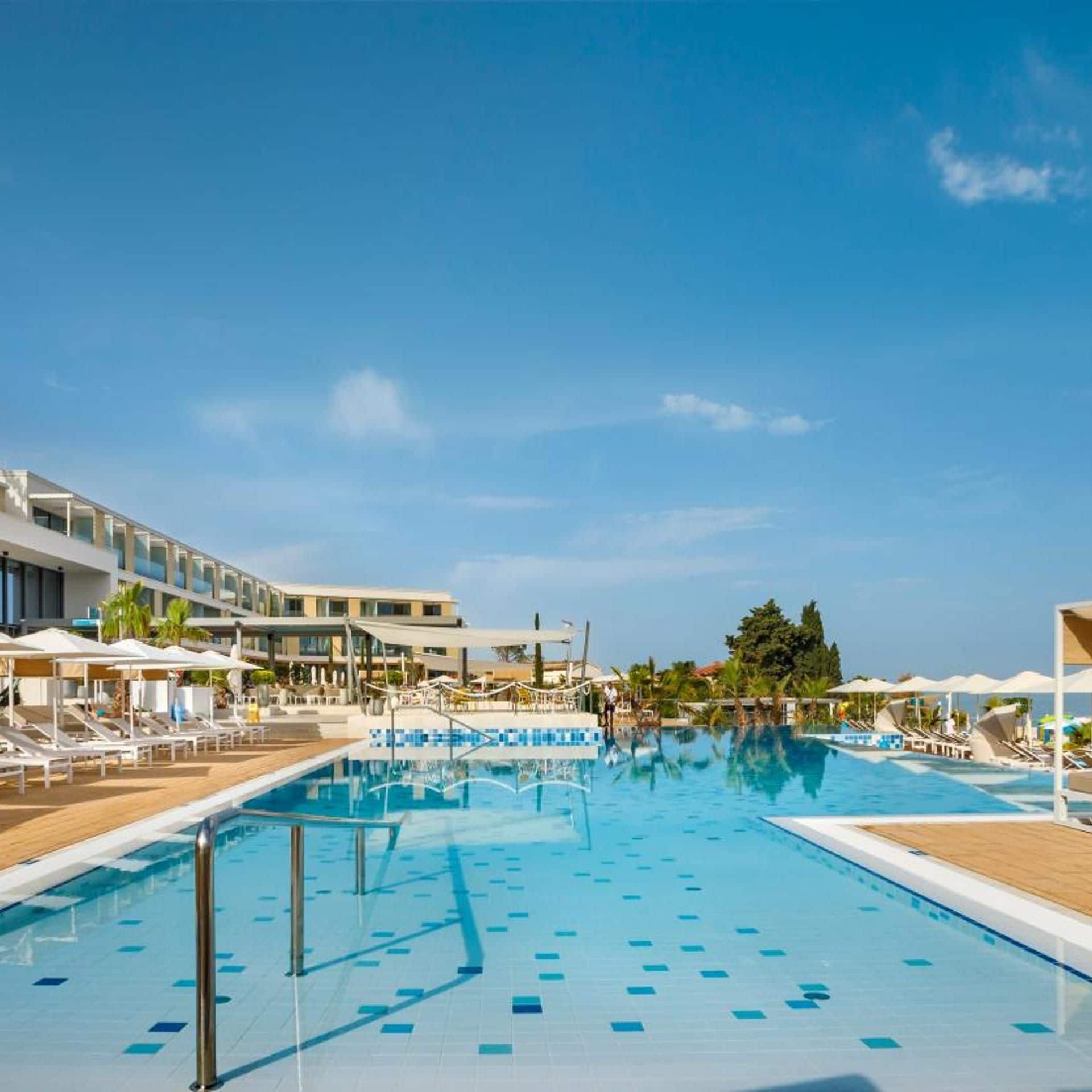 A swimming pool with lounge chairs and umbrellas, surrounded by a building with multiple floors.
