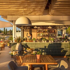 An outdoor bar area with a wooden table, chairs, and a variety of plants.