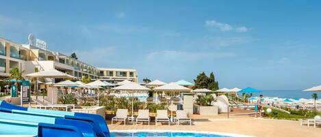 Une piscine d’hôtel avec un ciel dégagé, des chaises longues, des parasols et un bâtiment portant une enseigne.