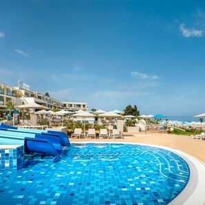 A hotel pool area with a clear sky, lounge chairs, umbrellas, and a building with a sign.