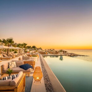 A resort pool area with lounge chairs and umbrellas, a pathway leading to the water, and a sunset view. - Marea Valamar Collection Suites (Porec)