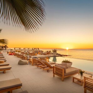 A beachfront lounge area with sun loungers, a pool, and a view of the sunset over the ocean. - Marea Valamar Collection Suites (Porec)