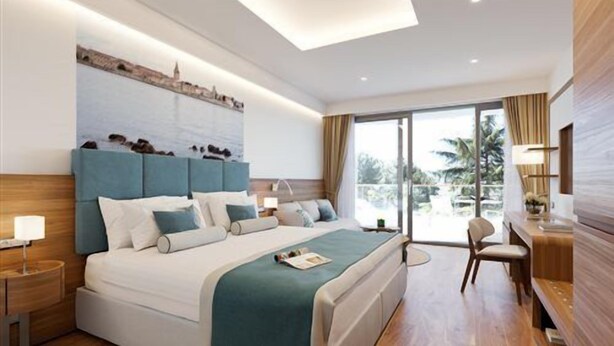 A modern hotel room with a large bed, bedside tables, a desk, and a view of the outdoors. - Marea Valamar Collection Suites (Porec)