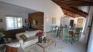 A spacious living area with a white sofa, a coffee table, and a dining area with green chairs. - Pousada Caminho das Aroeiras (Búzios)