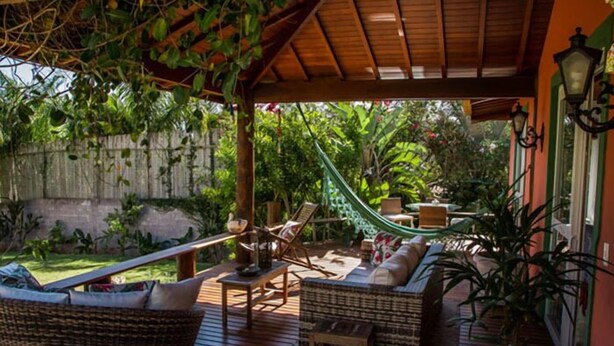 A wooden deck with wicker furniture, a hammock, and a potted plant. - Pousada Caminho das Aroeiras (Búzios)