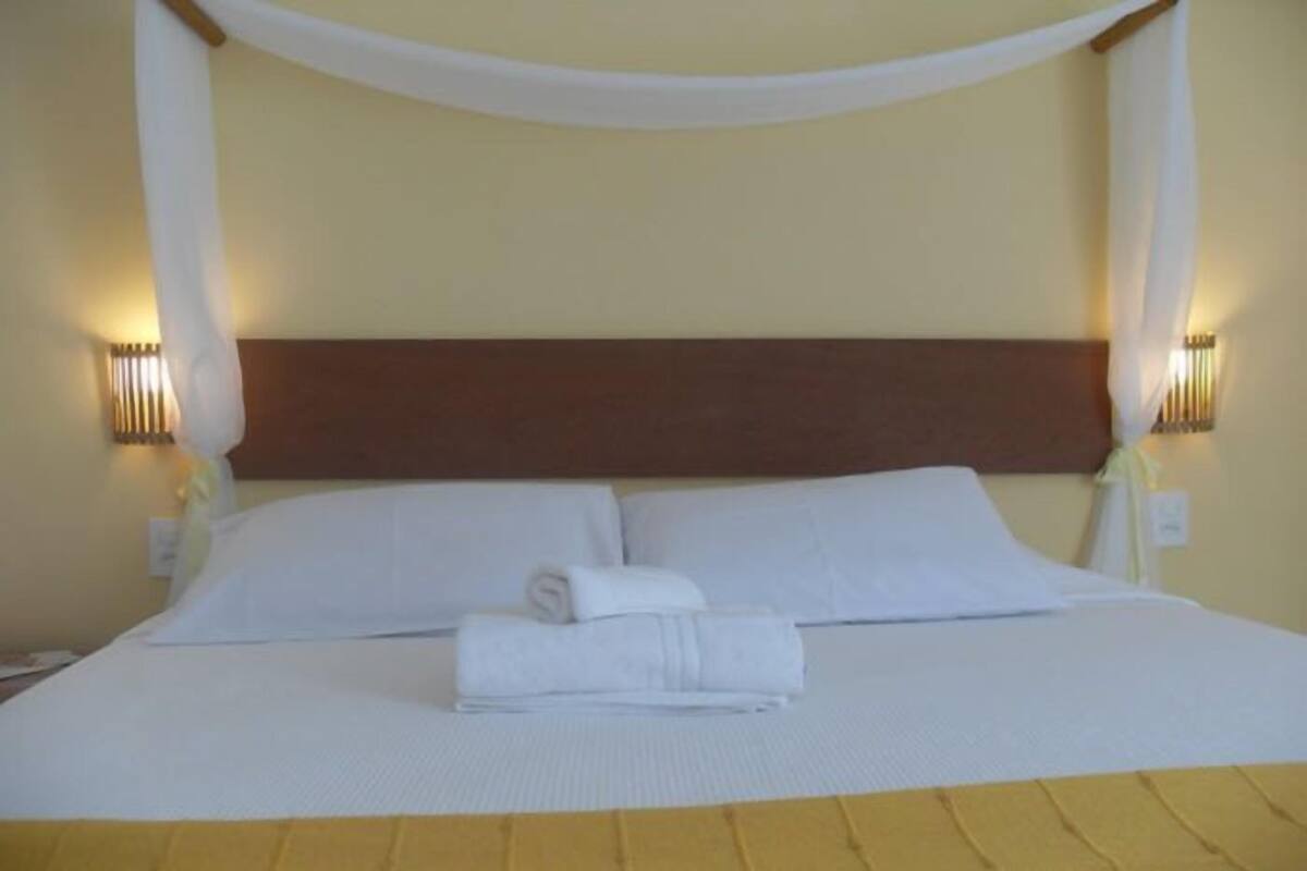 A neatly made bed with white linens and a wooden headboard, two bedside lamps, and a canopy.