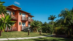 A two-story building with a red facade, balconies, and a well-maintained lawn with palm trees. - Pousada Caminho das Aroeiras (Búzios)